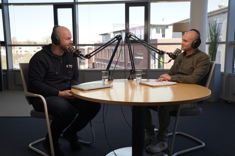 Ein Videopodcast Host unterhaltet sich mit einem Gast. Dabei sieht man das Podcast SetUp und Equipment