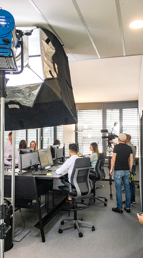 Behind-the-Scenes-Aufnahme von Deichblick-Filmteam das Personen an Bürotisch sitzend aufnimmt.