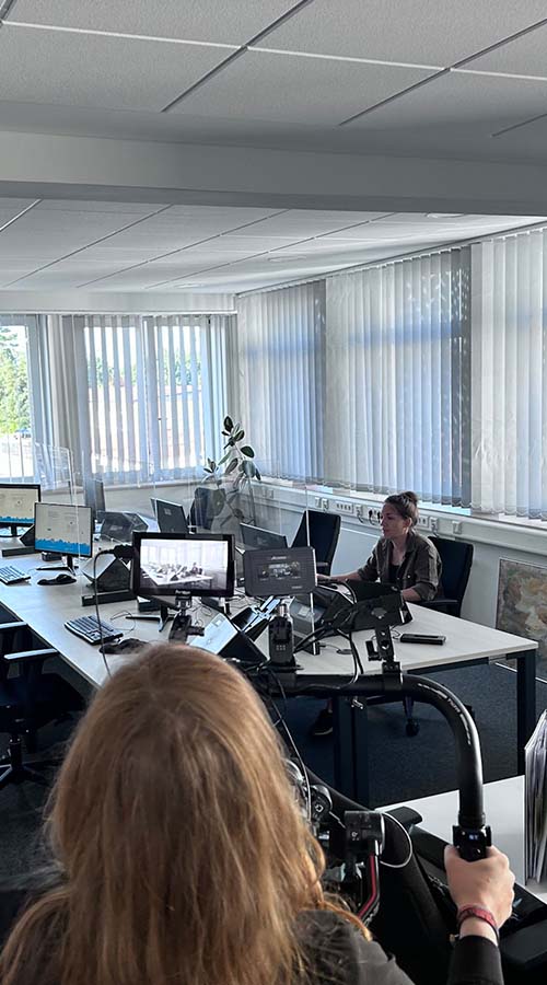 Großes Büro mit großem Tisch und sitzender Frau. Zwei Frauen im Vordergrund filmen Büroumgebung.